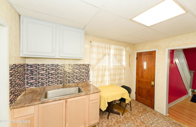 kitchen with a drop ceiling, a sink, light countertops, white cabinetry, and tasteful backsplash