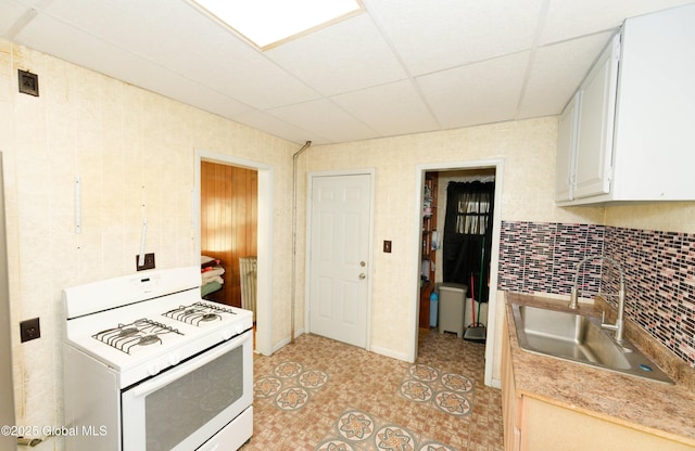 kitchen featuring backsplash, gas range gas stove, white cabinetry, a paneled ceiling, and a sink