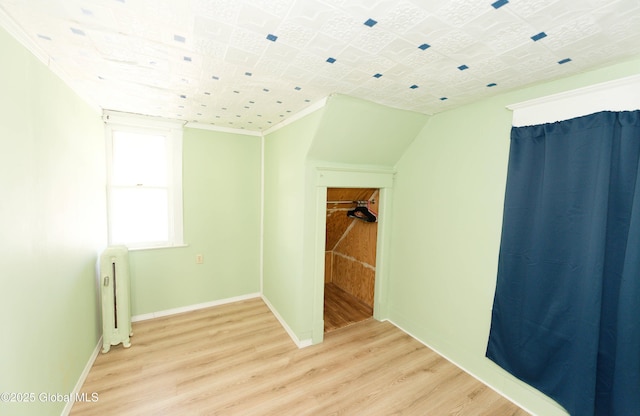 empty room featuring light wood-style flooring, radiator, crown molding, and baseboards