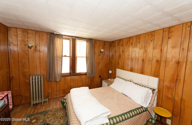 bedroom featuring wooden walls, radiator, and wood finished floors