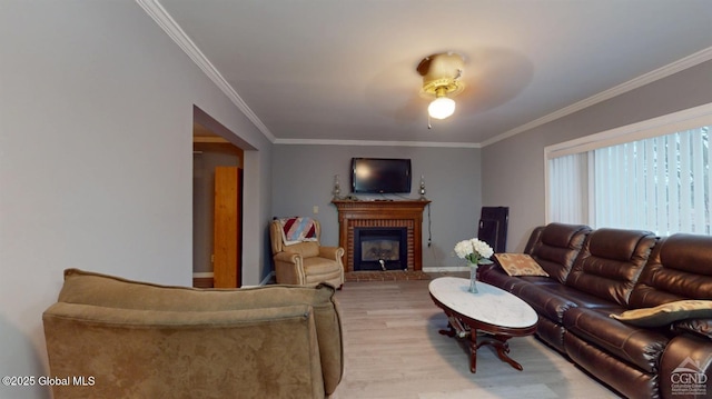 living area featuring ornamental molding, light wood-type flooring, and a brick fireplace