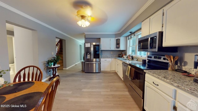 kitchen featuring light wood finished floors, crown molding, appliances with stainless steel finishes, and a sink