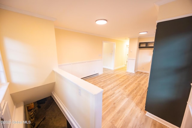 corridor featuring baseboards, ornamental molding, baseboard heating, and light wood-style floors