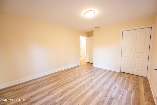 unfurnished bedroom with visible vents, baseboards, crown molding, light wood-style floors, and a closet