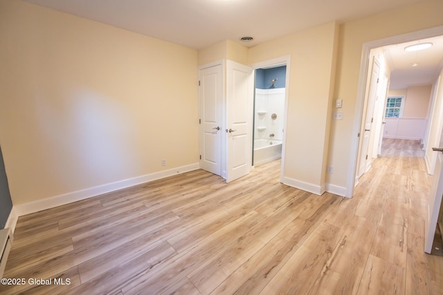 unfurnished bedroom featuring ensuite bathroom, light wood finished floors, a baseboard radiator, and baseboards