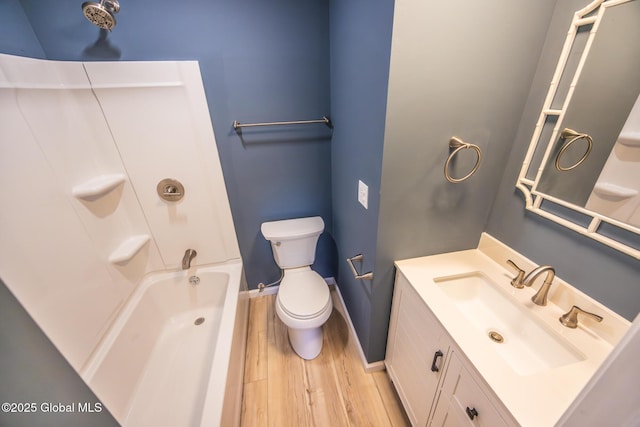 bathroom with toilet, wood finished floors, vanity, baseboards, and  shower combination