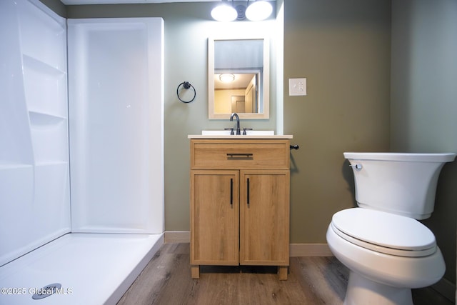 full bathroom with toilet, wood finished floors, vanity, baseboards, and a shower