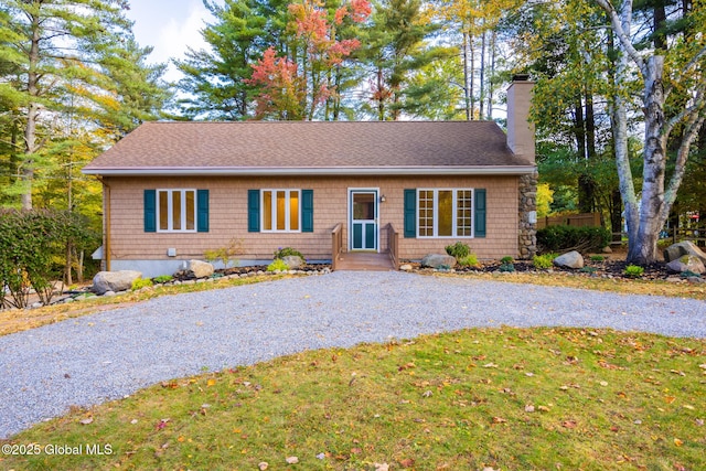 ranch-style home featuring roof with shingles, a chimney, gravel driveway, and a front yard