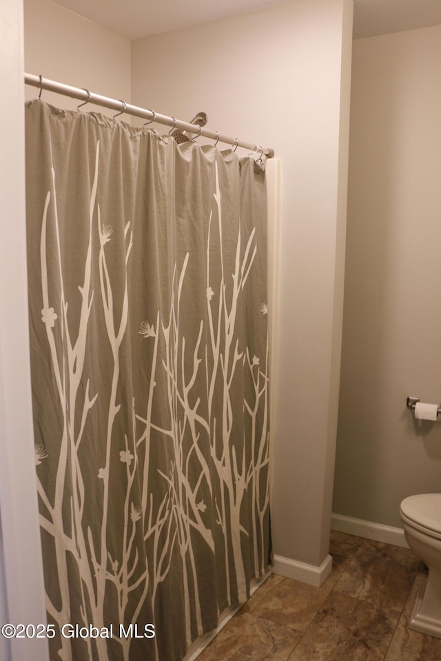 full bath featuring curtained shower, toilet, and baseboards