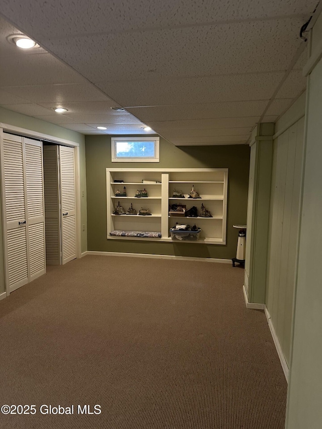 basement with built in features, a paneled ceiling, carpet flooring, and baseboards