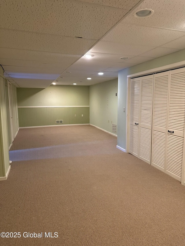 finished basement featuring carpet floors, baseboards, visible vents, and a drop ceiling