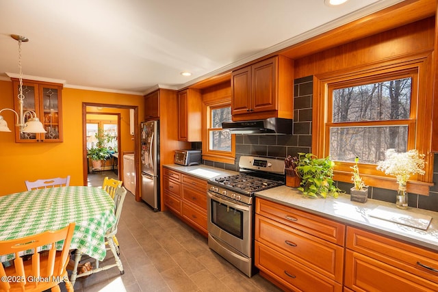 kitchen with brown cabinets, decorative light fixtures, backsplash, range hood, and stainless steel appliances