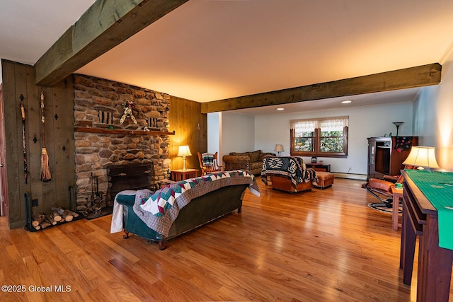 living area with a stone fireplace, beamed ceiling, a baseboard heating unit, and wood finished floors