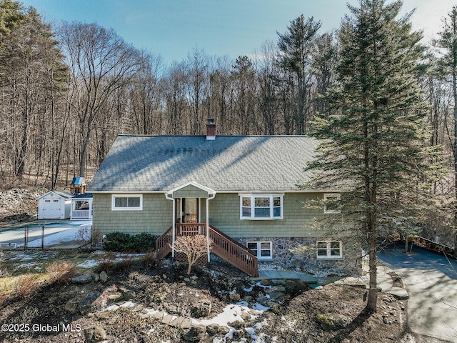 view of front of house featuring roof with shingles, an outdoor structure, and a chimney