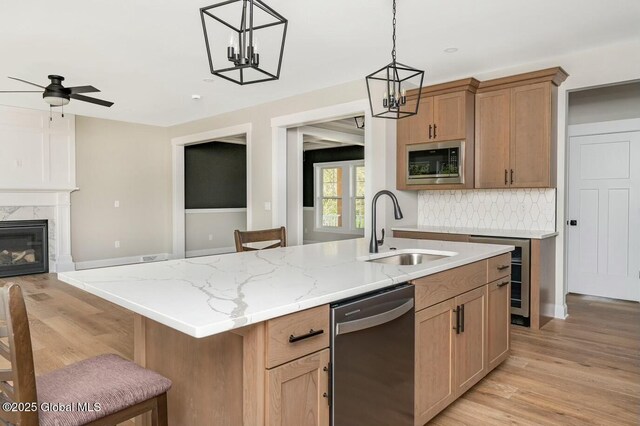 kitchen featuring light wood-style flooring, appliances with stainless steel finishes, a high end fireplace, a sink, and an island with sink