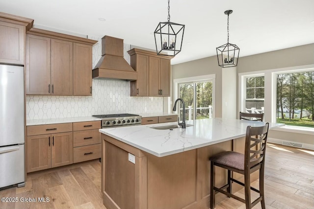 kitchen featuring custom exhaust hood, light wood-type flooring, a sink, and stainless steel refrigerator