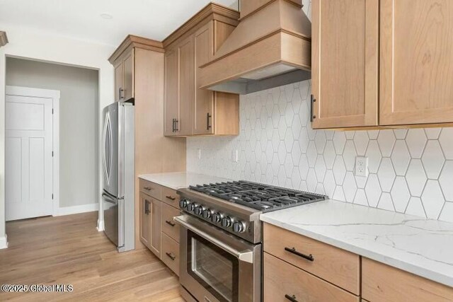 kitchen with light stone countertops, stainless steel appliances, decorative backsplash, light wood finished floors, and custom range hood