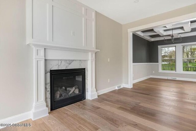 unfurnished living room with baseboards, coffered ceiling, beamed ceiling, light wood-type flooring, and a high end fireplace