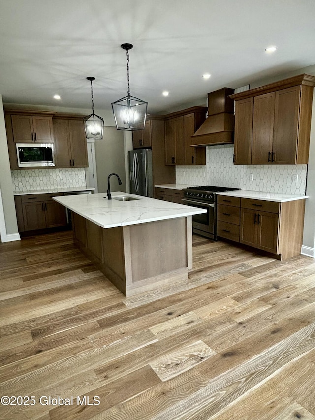 kitchen with a center island with sink, light wood-style flooring, custom range hood, stainless steel appliances, and a sink