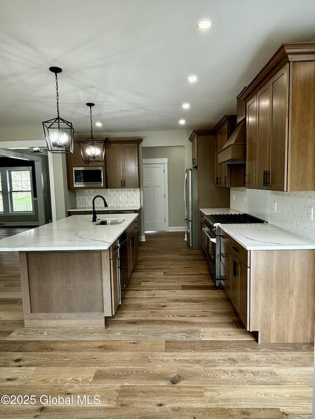 kitchen with tasteful backsplash, appliances with stainless steel finishes, light wood-style floors, a sink, and wall chimney exhaust hood