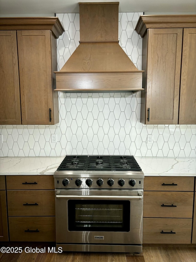 kitchen featuring tasteful backsplash, custom exhaust hood, brown cabinetry, and high end stainless steel range