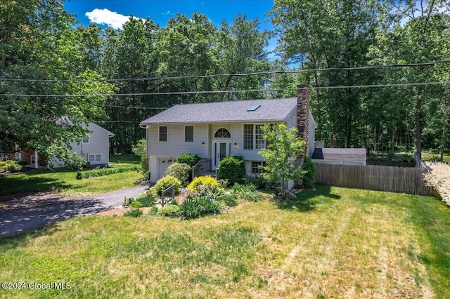 split foyer home with a garage, a shingled roof, driveway, a front lawn, and a chimney