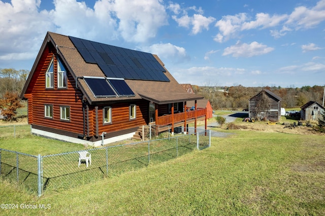 back of house featuring a shingled roof, log exterior, roof mounted solar panels, a lawn, and a fenced backyard