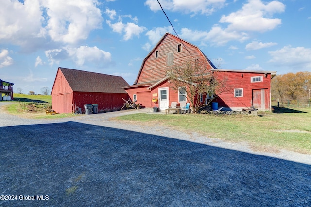 rear view of property featuring a gambrel roof, an outbuilding, driveway, a barn, and a yard