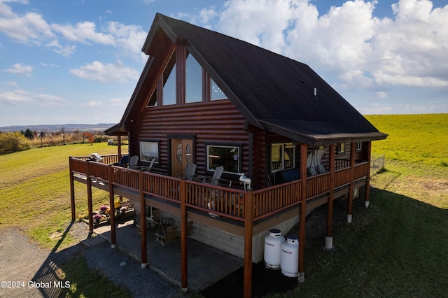 back of property featuring a yard, roof with shingles, a wooden deck, log siding, and a patio area