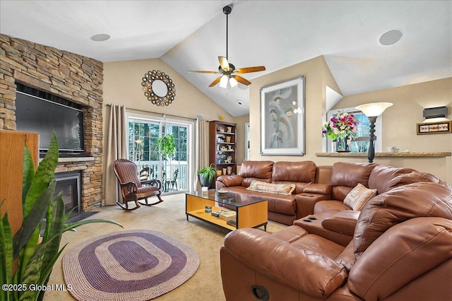 living area featuring light carpet, lofted ceiling, a stone fireplace, and a ceiling fan