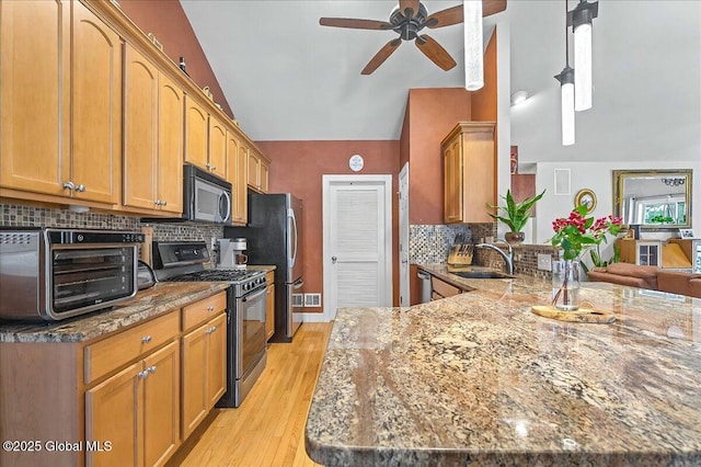 kitchen with a toaster, vaulted ceiling, appliances with stainless steel finishes, stone countertops, and a sink