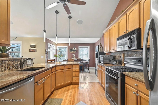 kitchen with vaulted ceiling, decorative backsplash, dark stone countertops, appliances with stainless steel finishes, and a sink