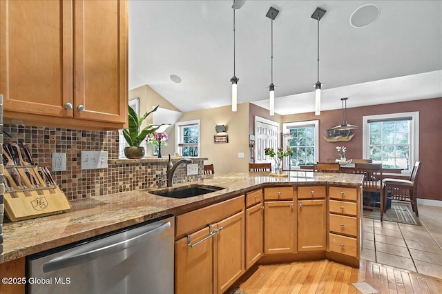 kitchen with light stone counters, a sink, stainless steel dishwasher, decorative light fixtures, and backsplash