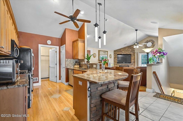 kitchen with stone counters, a peninsula, a sink, appliances with stainless steel finishes, and a kitchen breakfast bar