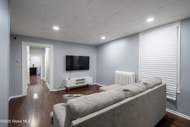 living area featuring a drop ceiling, baseboards, radiator heating unit, and dark wood-type flooring