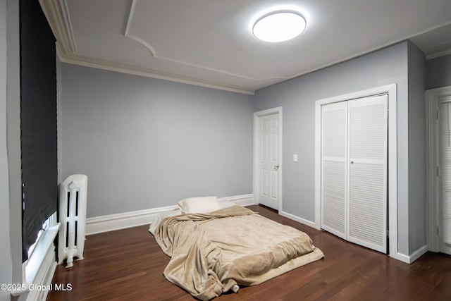 bedroom featuring radiator heating unit, a closet, crown molding, baseboards, and dark wood-style flooring