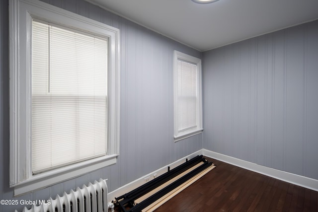 unfurnished room featuring baseboards, dark wood-type flooring, and radiator heating unit