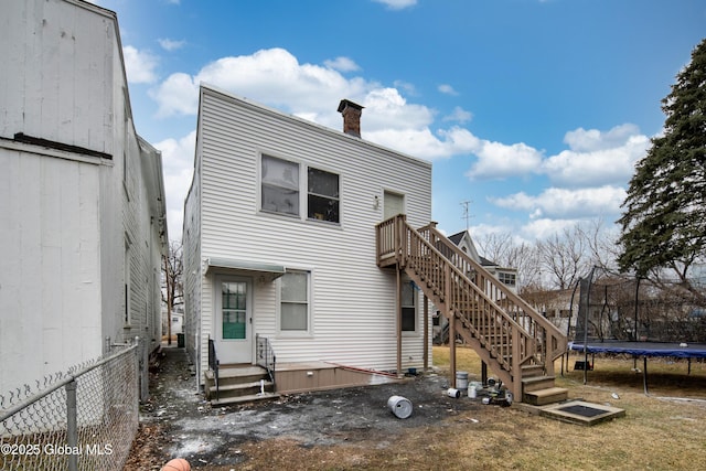 back of house with stairway, a trampoline, a chimney, and fence