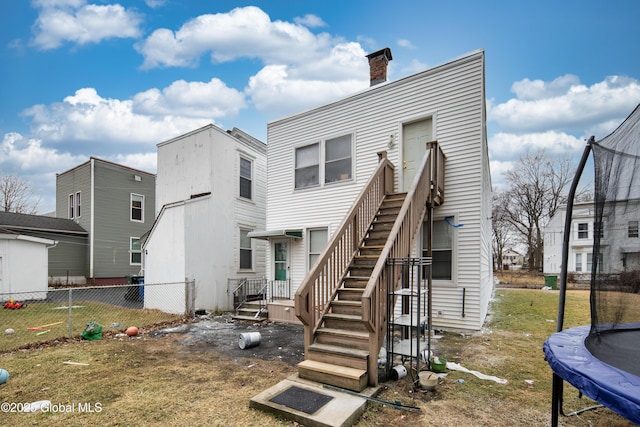 back of house with stairway, a trampoline, a chimney, and fence