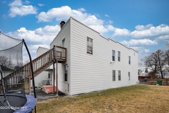 view of side of home featuring a trampoline, stairway, a wooden deck, a lawn, and a chimney