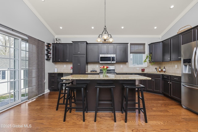 kitchen with a kitchen island, crown molding, a kitchen bar, appliances with stainless steel finishes, and wood finished floors