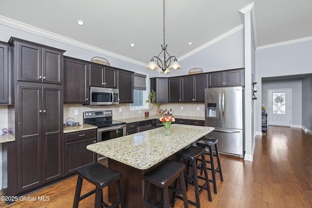 kitchen with a kitchen island, dark wood-style flooring, decorative backsplash, appliances with stainless steel finishes, and a kitchen breakfast bar