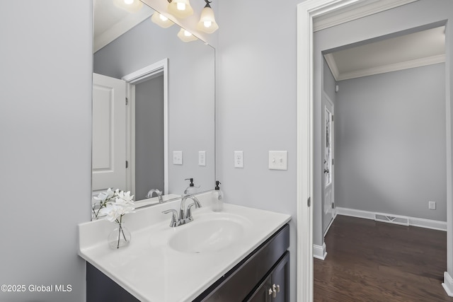 bathroom featuring baseboards, wood finished floors, ornamental molding, and vanity