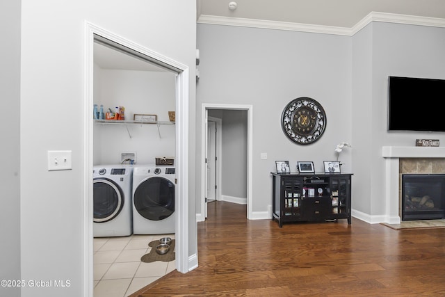 washroom with washing machine and clothes dryer, crown molding, a tiled fireplace, laundry area, and wood finished floors