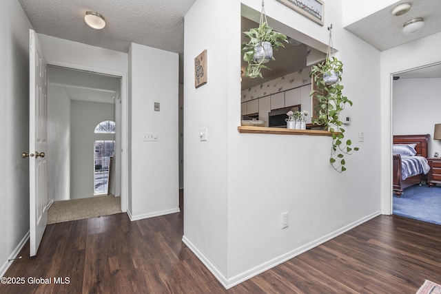 corridor featuring a textured ceiling, baseboards, and wood finished floors