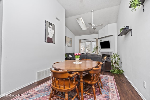 dining room featuring visible vents, vaulted ceiling with skylight, wood finished floors, and a fireplace