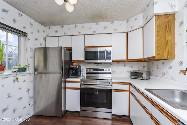 kitchen with wallpapered walls, a textured ceiling, white cabinetry, and stainless steel appliances