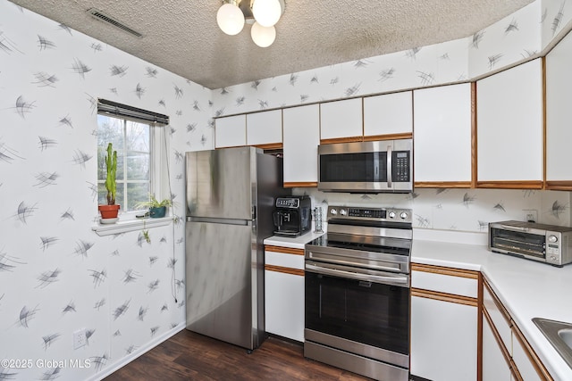 kitchen with visible vents, wallpapered walls, a textured ceiling, appliances with stainless steel finishes, and light countertops