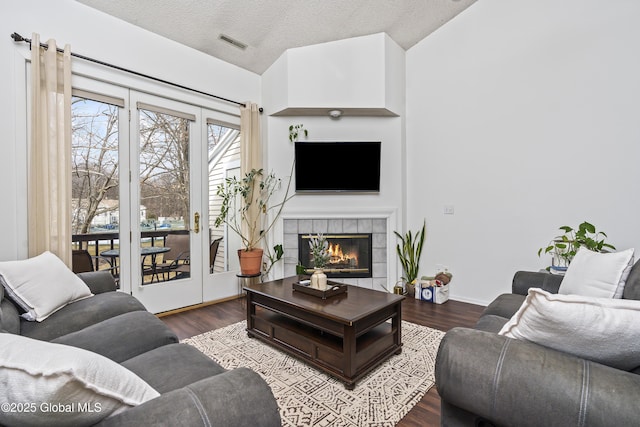 living area featuring visible vents, a textured ceiling, wood finished floors, and a tiled fireplace