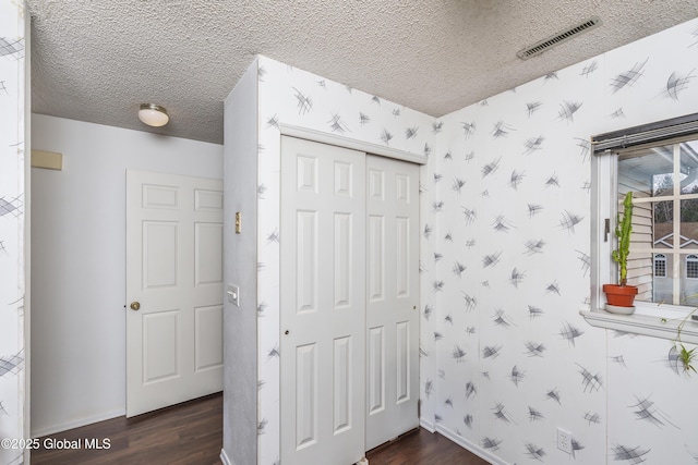 bedroom with wallpapered walls, visible vents, dark wood-style flooring, and a textured ceiling